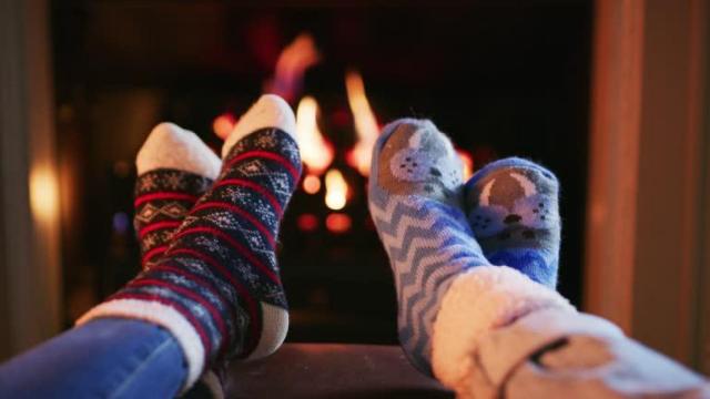 Dos personas calentándose los pies en la chimenea.