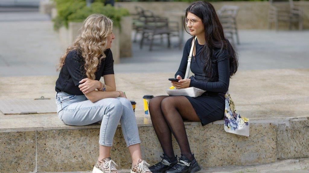 Dos jóvenes hablando sentadas en la calle.