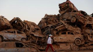 Una persona camina delante de un conjunto de coches apilados un mes después de las inundaciones.