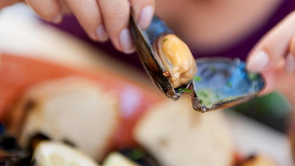 Imagen de una mujer con un mejillón en la mano.
