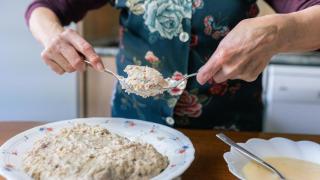 Una mujer rebozando croquetas utilizando dos cucharas de cocina.