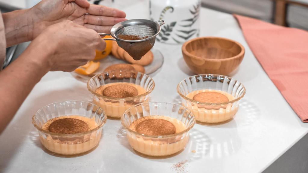 Una persona espolvorea canela por encima de unas natillas.