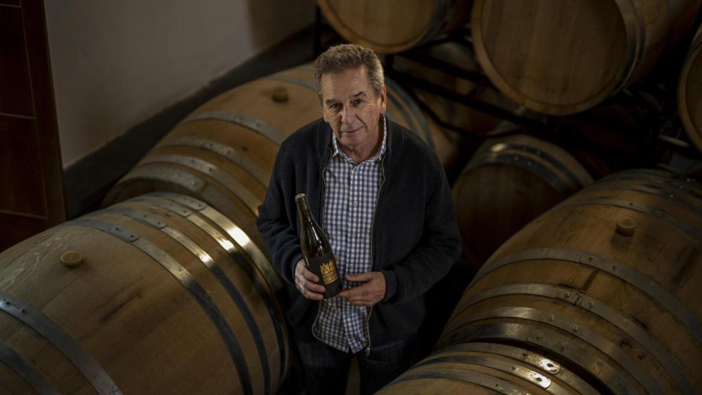 Antonio López Fernández sostiene en sus manos una botella de la variedad de uva blanca Godello mientras posa entre barricas de roble francés en la bodega de Alvaredos-Hobbs.