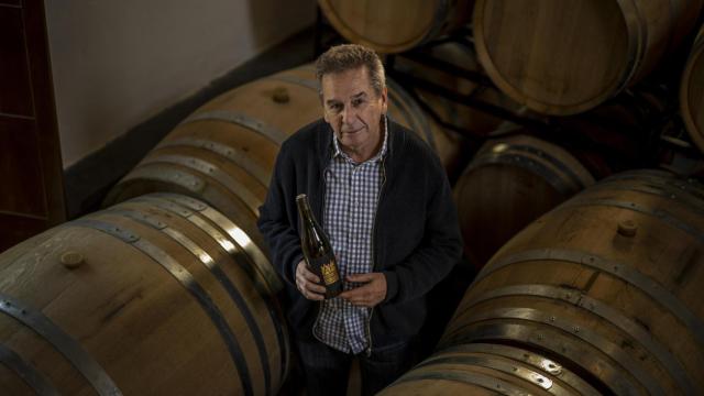 Antonio López Fernández sostiene en sus manos una botella de la variedad de uva blanca Godello mientras posa entre barricas de roble francés en la bodega de Alvaredos-Hobbs.
