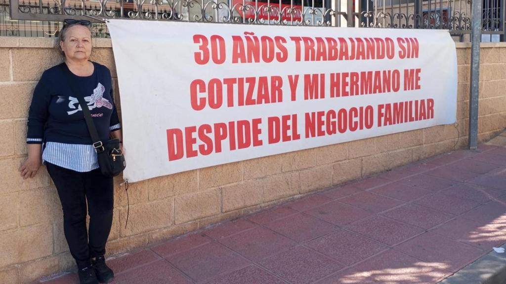 Antonia Asensio, de 65 años, posando con una de sus pancartas de protesta contra su hermano, en la fachada de la tienda de recambios de automoción en Sangonera la Seca.