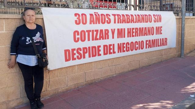 Antonia Asensio, de 65 años, posando con una de sus pancartas de protesta contra su hermano, en la fachada de la tienda de recambios de automoción en Sangonera la Seca.