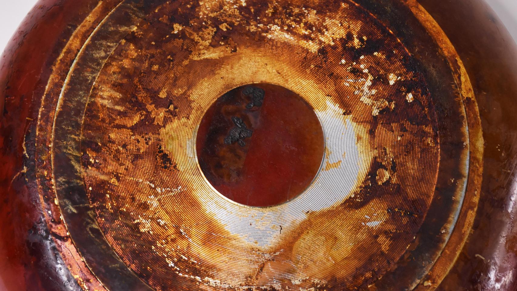 Una sartén vista desde abajo, mostrando una gruesa capa de grasa y suciedad acumulada en su base.