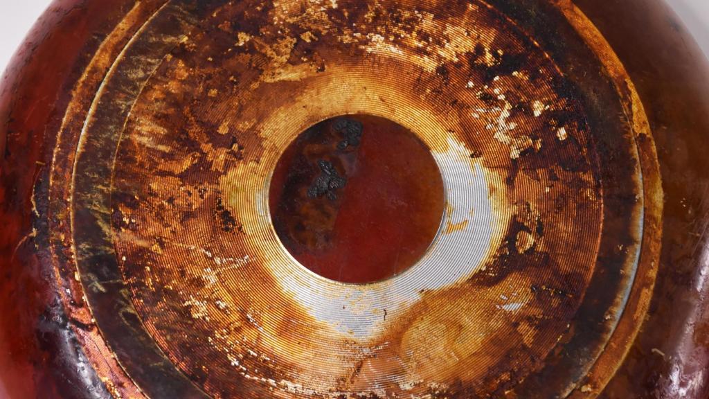 Una sartén vista desde abajo, mostrando una gruesa capa de grasa y suciedad acumulada en su base.