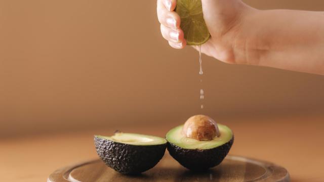 Primer plano de una mano exprimiendo un limón sobre un aguacate cortado.