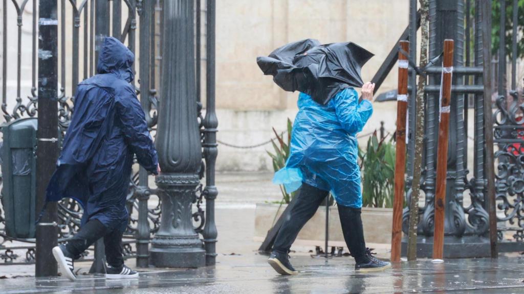 Dos personas se protegen de la lluvia de Sevilla con chubasqueros de plástico.