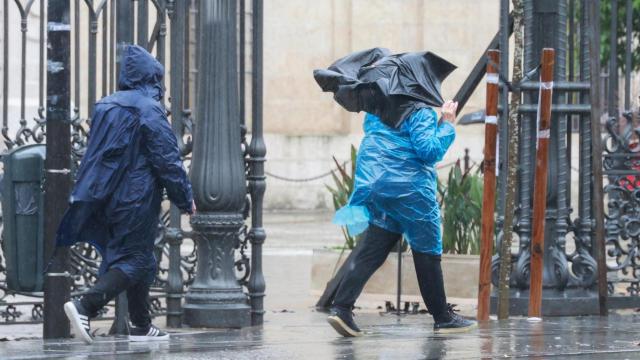 Dos personas se protegen de la lluvia de Sevilla con chubasqueros de plástico.