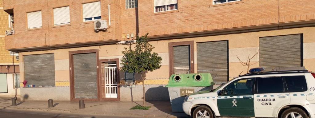 Una patrulla de la Guardia Civil, este jueves, aparcada en el bar de Torreagüera donde Sebastián mató de un disparo a Alicia, al fondo, en la fachada del local, un ramo de flores y varias velas colocadas por los familiares de la fallecida.
