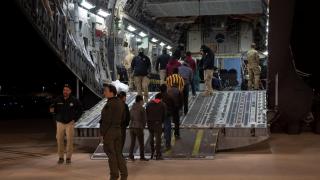 Agentes fronterizos montan en un avión de la Fuerza Aérea a una cuerda de inmigrantes detenidos para deportarlos.