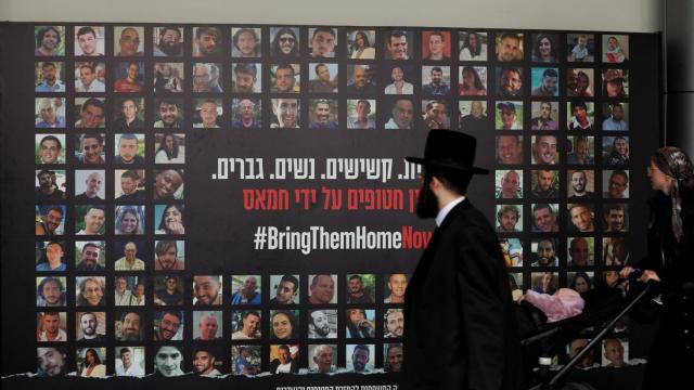 Un judío ultraortodoxo observa un  mural en Tel Aviv con los rostros de los rehenes tomados por Hamás en los ataques del 7 de octubre.