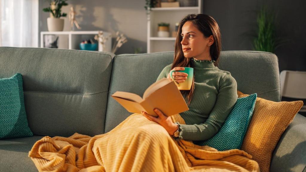 Mujer leyendo en el sofá con una taza de café.