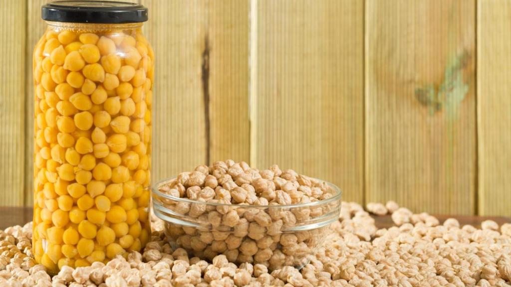 Garbanzos en un bote de cristal junto a un cuenco de garbanzos crudos.