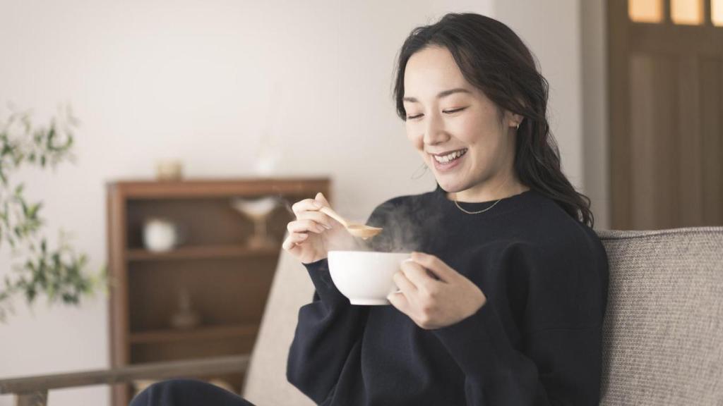 Mujer asiática tomando sopa en el sofá.