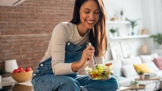 Mujer comiendo una ensalada sobre la encimera de la cocina.