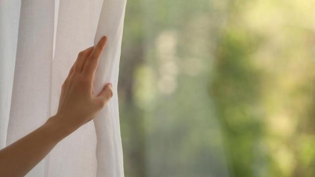 Una mujer abriendo cortinas blancas.