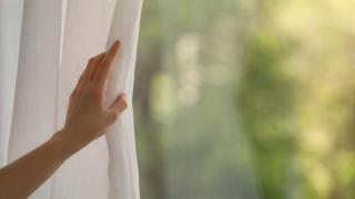 Una mujer abriendo cortinas blancas.