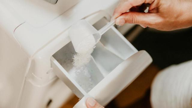 Una mano vertiendo detergente en polvo en el compartimento de la lavadora.