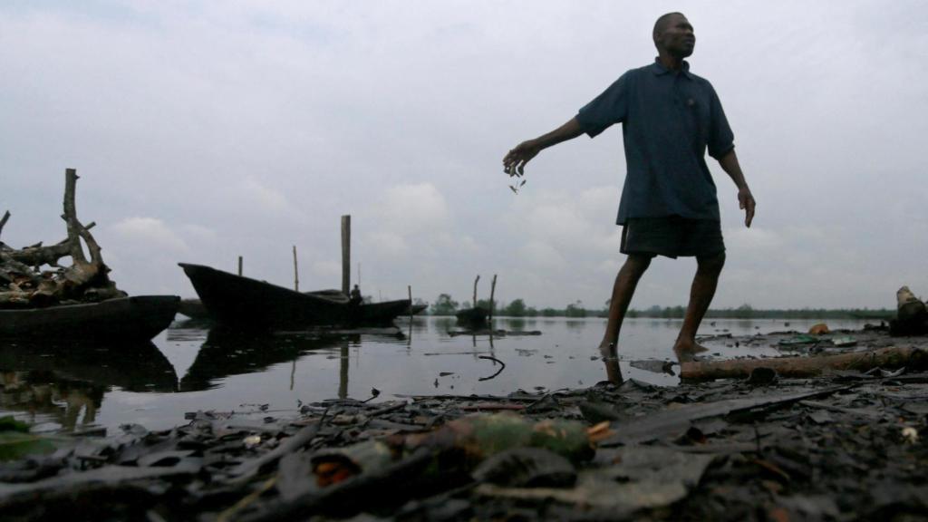 Un hombre arroja peces muertos a un río contaminado en Ogoniland, estado de Rivers, Nigeria, el 18 de septiembre de 2020.