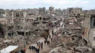 Un grupo de palestinos caminan entre el barro y los escombros de edificios destruidos por Israel.