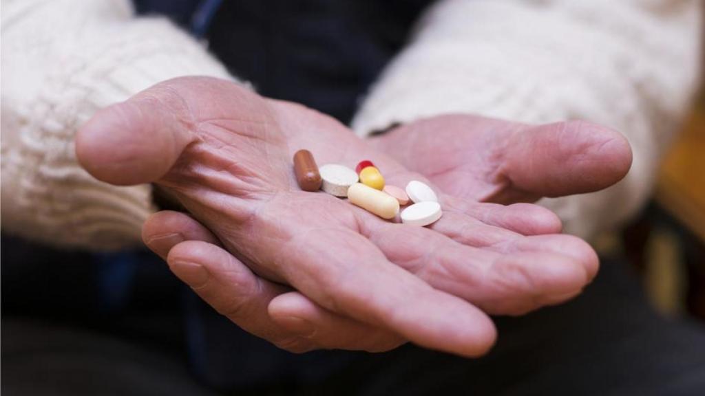 Un anciano sostiene distintos medicamentos en sus manos.