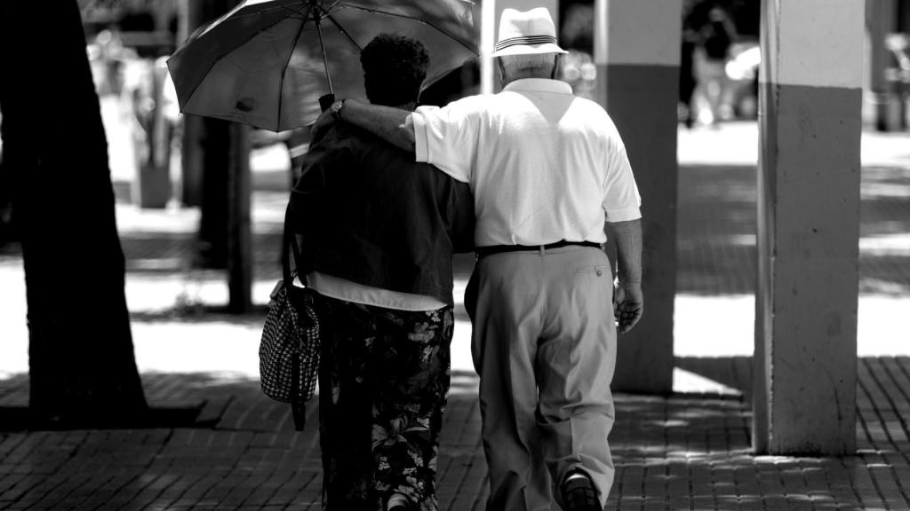 Dos personas mayores caminan bajo la sombra de un árbol