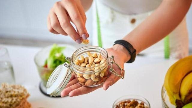 Mujer cogiendo frutos secos de un recipiente de cristal.