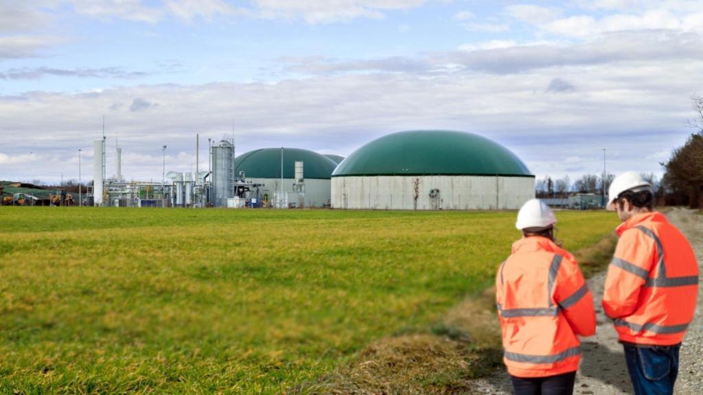 Imagen de dos operarios y, al fondo, una planta de biometano.