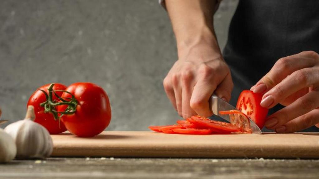 Mujer cortando tomates frescos sobre una tabla.