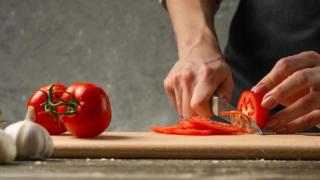 Mujer cortando tomates frescos sobre una tabla.