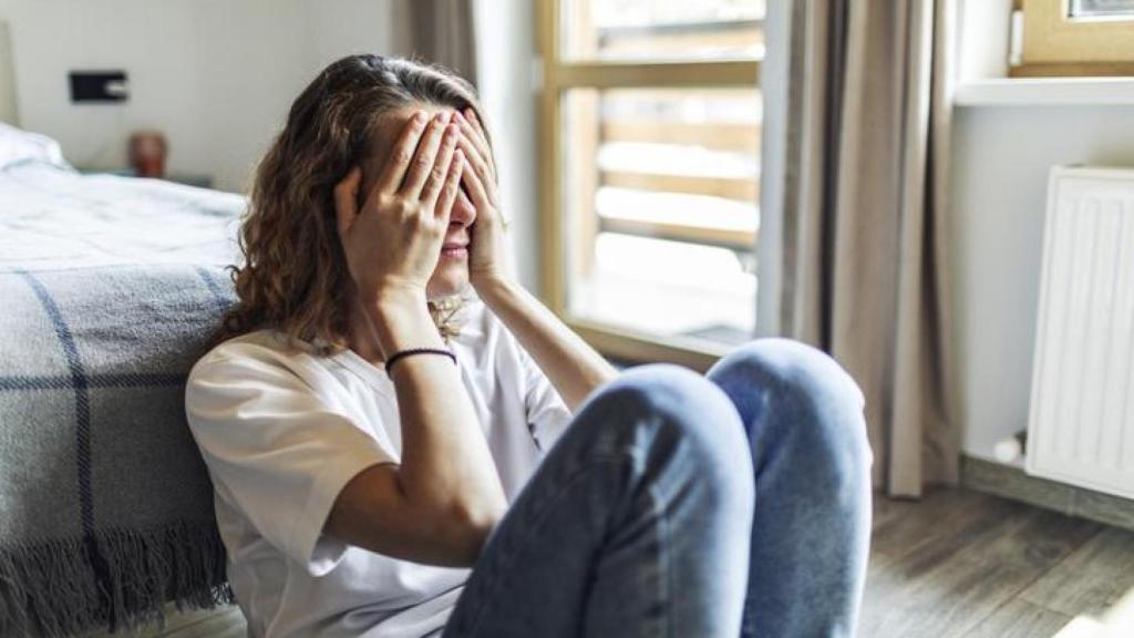 Mujer sentada en el suelo tapándose la cara con las manos.