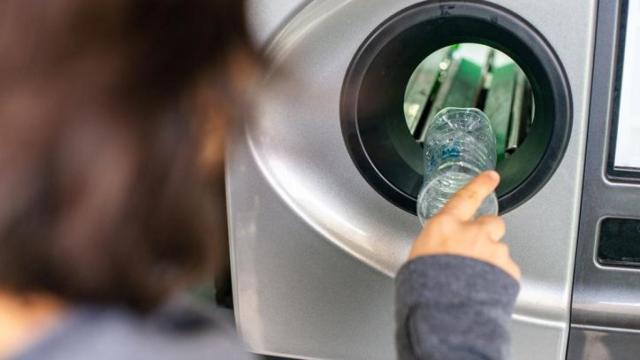 Una mujer depositando la botella en una máquina del sistema de devolución.