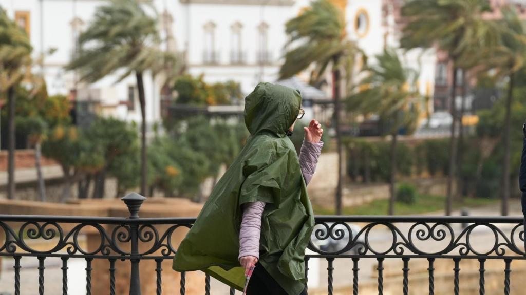 Una persona se protege de la lluvia con un chubasqueros mientras cruza el Puente de Triana.