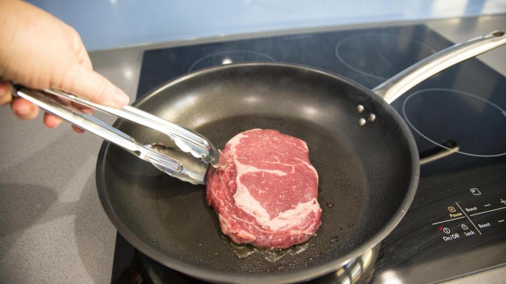 Una persona cocina un filete a la plancha (Imagen de archivo)