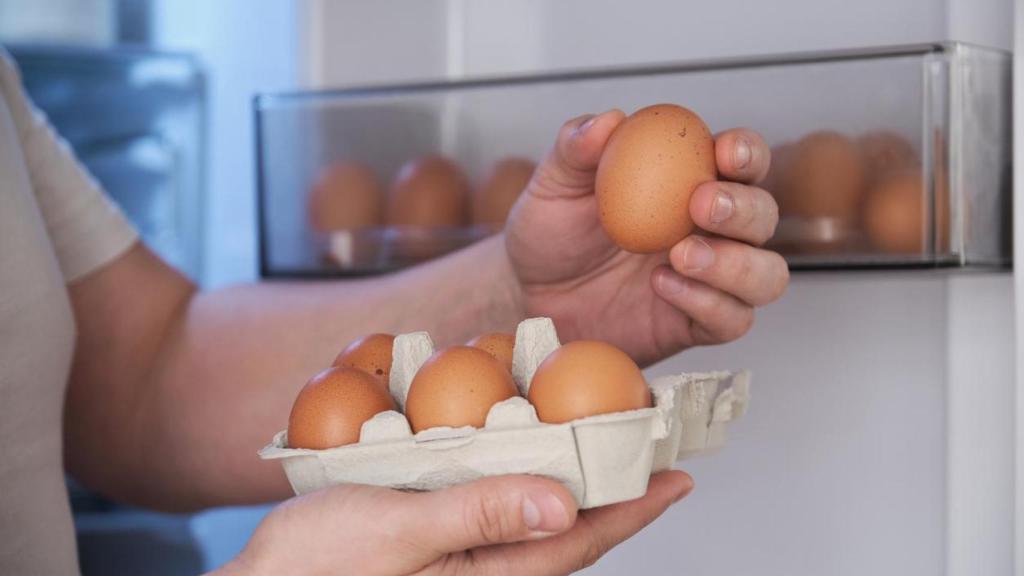 Primer plano de un hombre guardando huevos en la puerta del refrigerador.