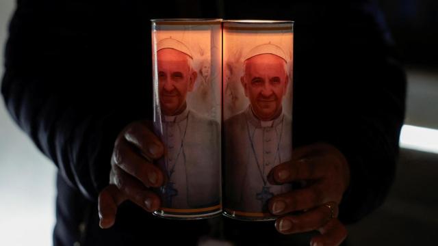 Un hombre sujeta velas con la imagen del papa a las puertas del hospital en el que estuvo ingresado en Roma.