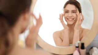 Mujer joven aplicándose crema frente al espejo.