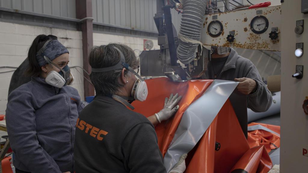 En la imagen, los trabajadores están en el proceso de termosellado o soldadura de alta frecuencia, uniendo piezas de PVC o Hypalón para fabricar los flotadores de una embarcación neumática.