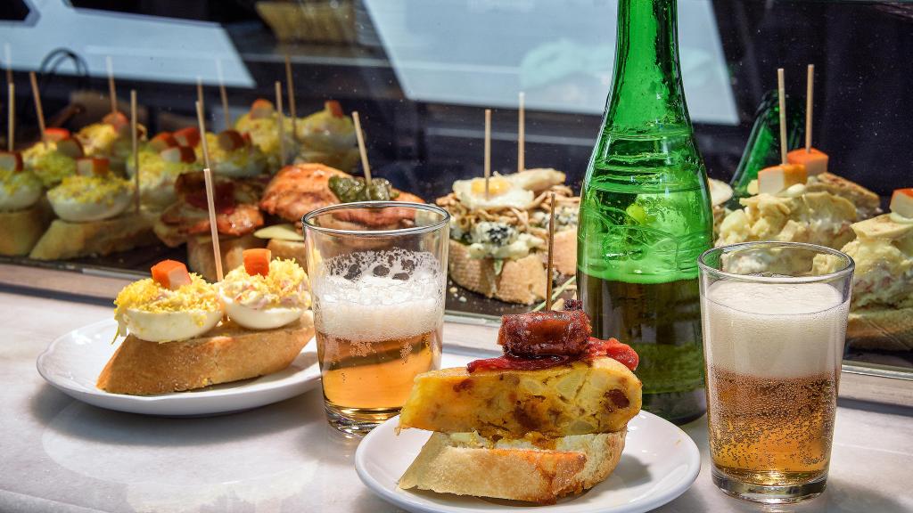 Barra de bar con cervezas y una variedad de pinchos españoles.