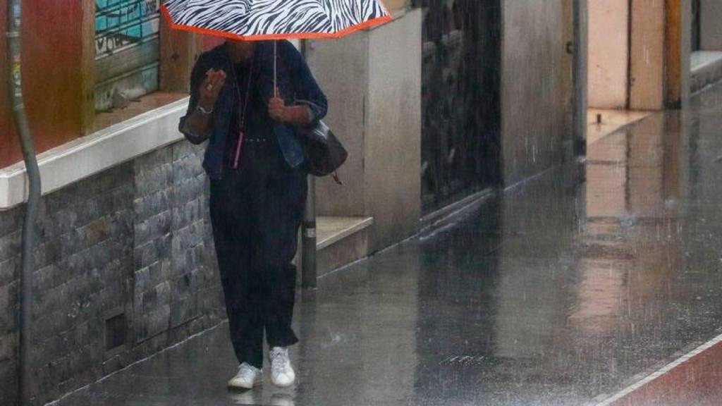 Una mujer se protege de una intensa lluvia con su paraguas.