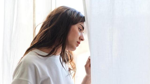 Mujer con aspecto preocupado mirando por la ventana.