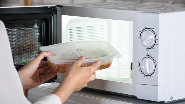 Una persona sacando un plato de comida del microondas.