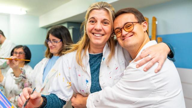 Un joven con Síndrome de Down abraza a su profesora de pintura.