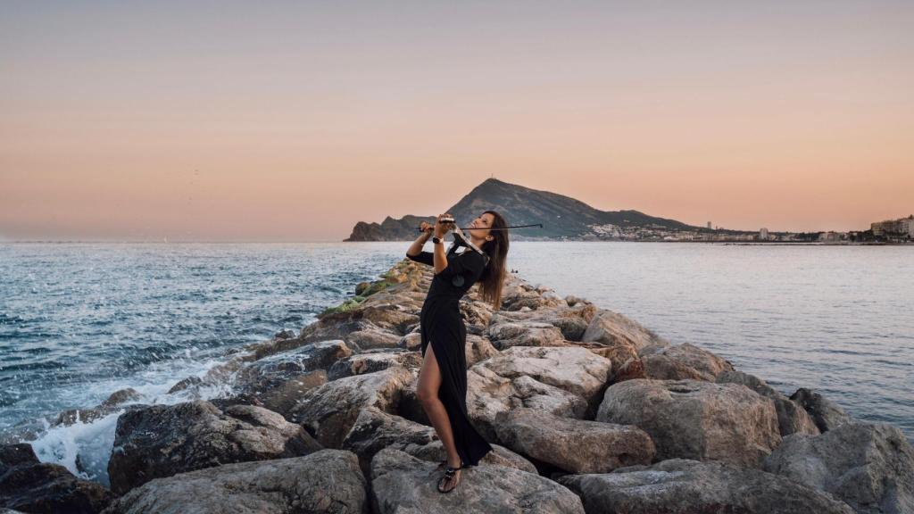 Clara Saval tocando entre las rocas con el mar de fondo