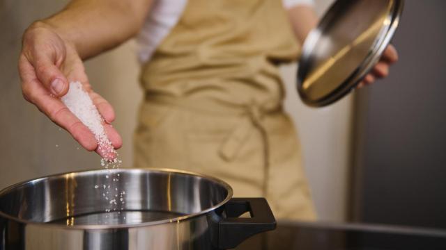 Una persona añadiendo sal a una olla con agua. (Imagen de archivo)