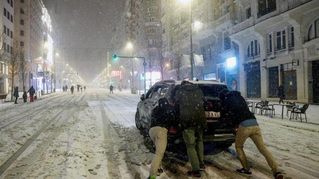 Jóvenes empujan un coche bajo la nieve en la Gran Vía de Madrid.