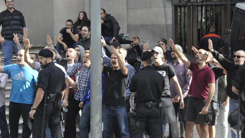 Al fondo, sentado con gafas de sol, junto a un grupo que hace el saludo fascista.